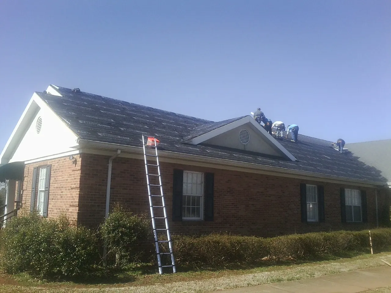 Crew tearing shingles off a brick ranch roof with a ladder set — Emergency Roof Repair work by our crew in Reynoldsburg