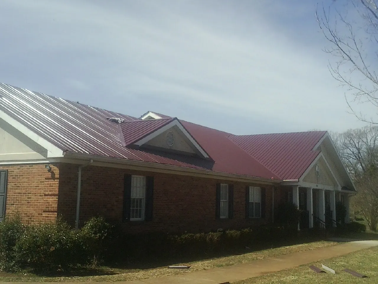 Red metal roof with gabled entries on a long brick building, from a Hail Damage Roof Repair job in Reynoldsburg
