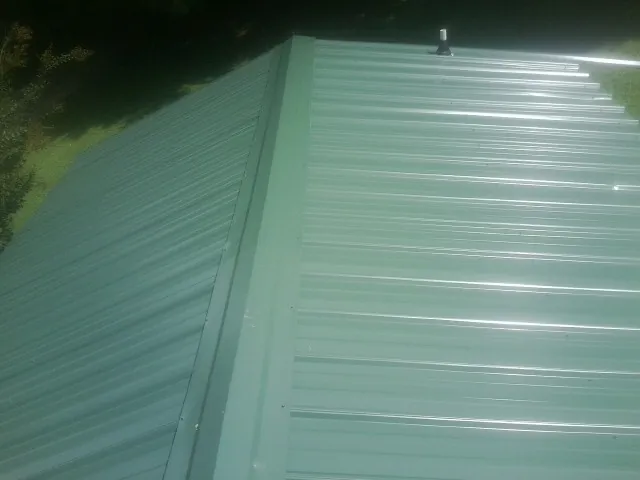 New green metal panels meeting at the ridge of a roof — Flat Roof Repair work by our crew in Reynoldsburg