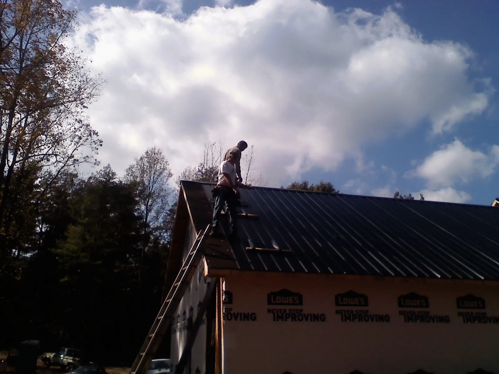 Roofer fastening dark metal panels high against a cloudy sky, from a Roof Inspection job in Reynoldsburg