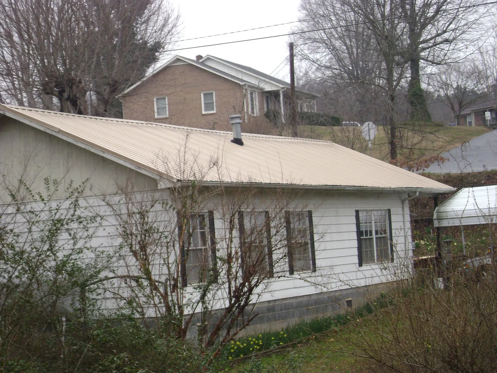 Tan metal roof on a white sided house set into a hillside — Commercial Roofing by Roofing Brothers in Reynoldsburg
